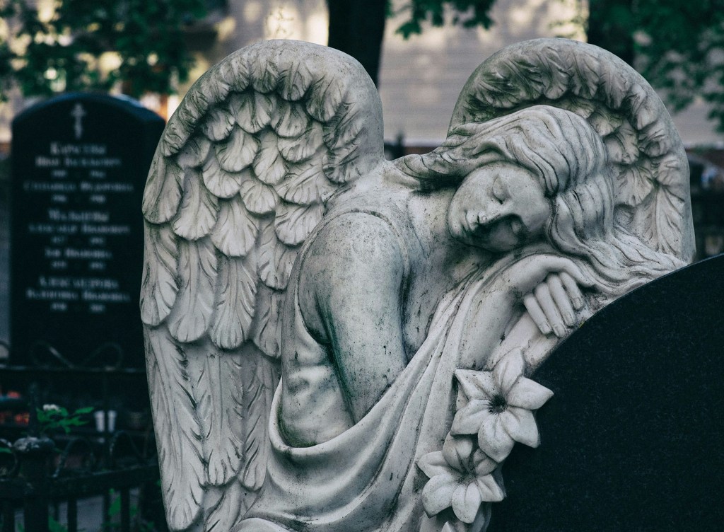 A grey angel headstone, the wings forming almost a heart shape. Very Victorian, with the angel resting eyes closed, standing but leaning